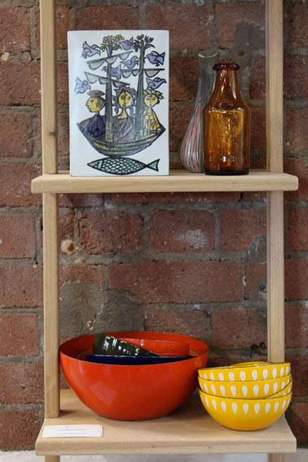 shelves with midcentury modern items including vintage Catherineholm enamel bowls and folk art tile