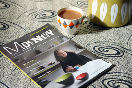 image of the front cover of the 1st edition of Midcentury Magazine pictured with a vintage Cathrineholm kettle and vintage harlequin china cup & saucer all on a piece of 1950s monochrome Crabtree fabric with milky way pattern