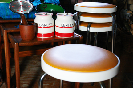 selection of recently acquired vintage items including a G Plan nest of teak tables, orange seated Chair Centre stacking stools, green & blue striped curtains, Rhythm pedestal clock, Scandinavian teak mortar & pestle, Hinomoto vinyl camera bag and red & white Kleen Kitchen Ware jars
