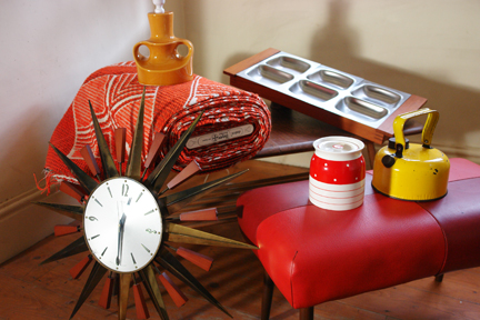 selection of vintage homewares recently acquired by H is for Home including a bolt of vintage orange Draylon fabric, Metamec starburst clock, bright yellow camping kettle, Old Hall teak & stainless steel serving dish, red & white polka dot Kirkham Pottery lidded pot, 1950s footstool with red vinyl seat, vintage yellow glazed pottery lamp base