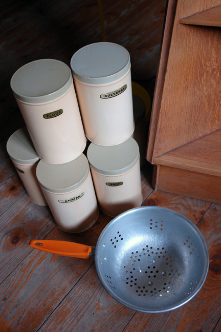 set of 1950s cream coloured kitchen storage tins with an orange-handled aluminium colander