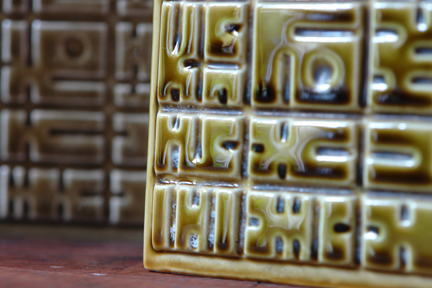 detail from pair of small, olive green, cube-shaped vintage Poole Pottery lamp bases with geometric pattern decoration detail from pair of small, olive green, cube-shaped vintage Poole Pottery lamp bases with geometric pattern decoration